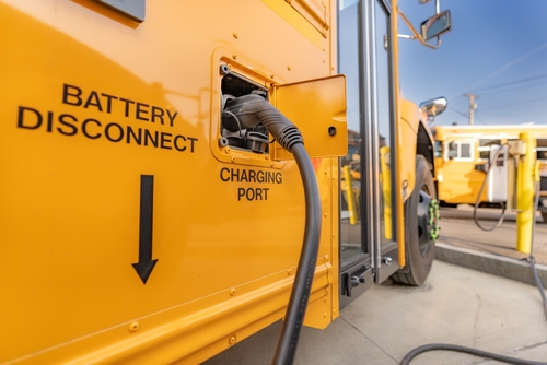 Photo of the side of an electric school bus, with a charging cord attached to the bus' charging port