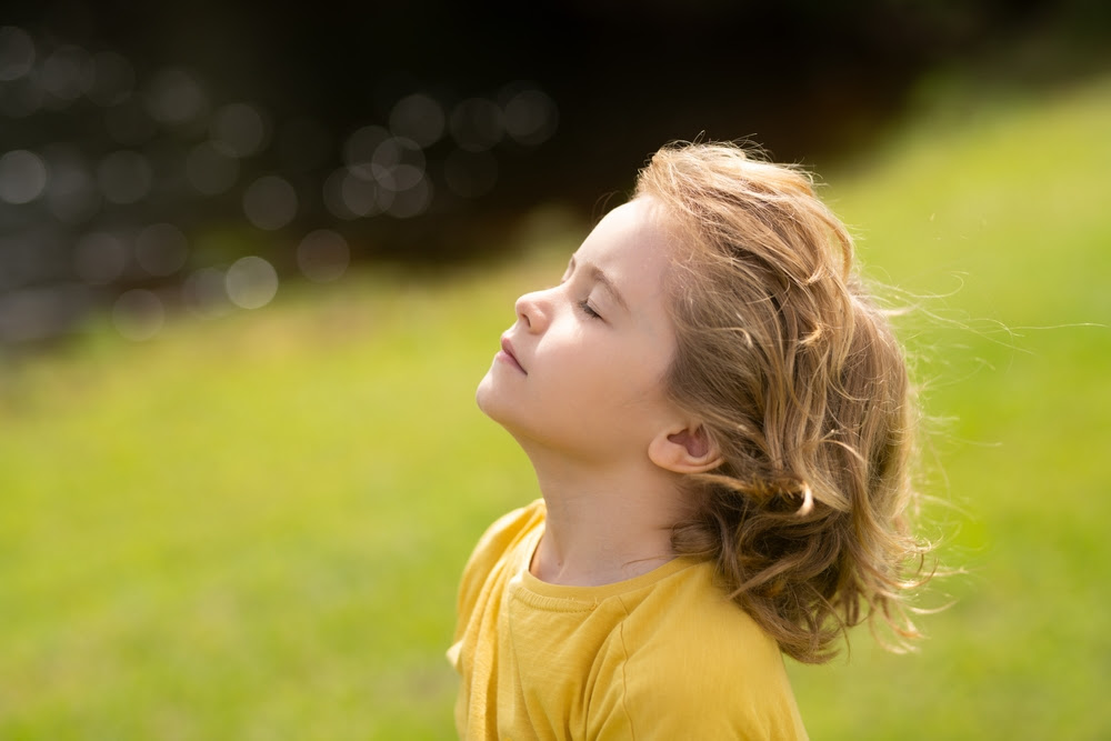Photo of a small girl in a field, head up, eyes closed, enjoying the feeling of the sun on her face