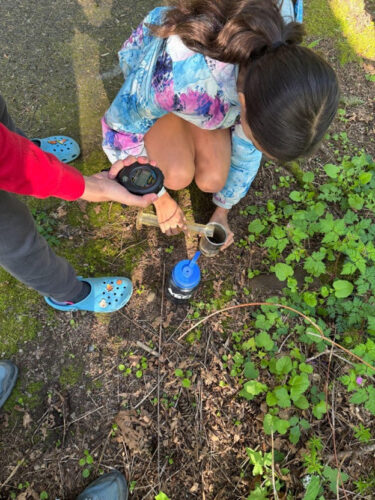 Photo of one student pouring water into a flask for testing, and another student using a measurement device on the water