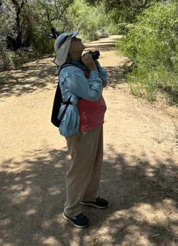 Photo of Mary Ratcliff, standing on a path in a forest, looking up at birds