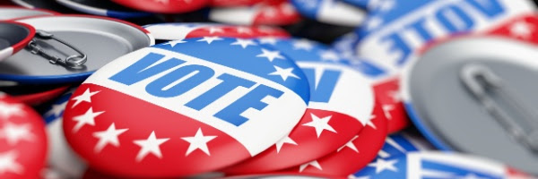 Photo of a pile of pins with the word "Vote" on them