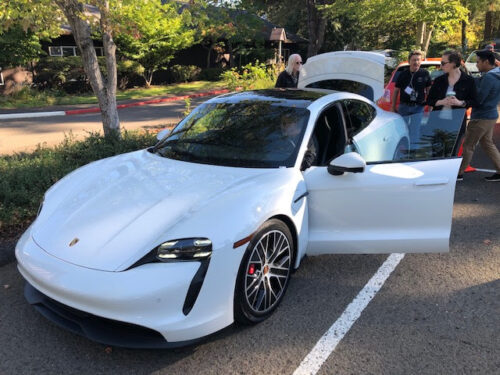 Photo of a parked white Porsche EV with its doors and trunk open