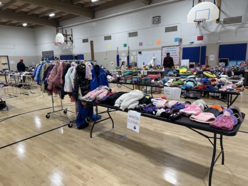 Photo showing piles of clothes on tables, and shoes under the tables